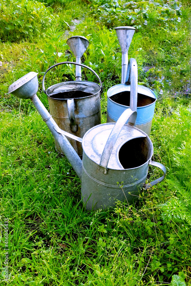 Three old rustic watering cans in the garden on green grass. Spring photo garden work. Three old rustic watering cans in the garden on green grass. Spring photo garden work.