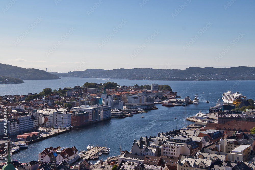 Panoramic view of Bergen. Horizontal view of the harbor and fiords in the background. Norwegian flag waving in the wind. View of the city center from mountain.