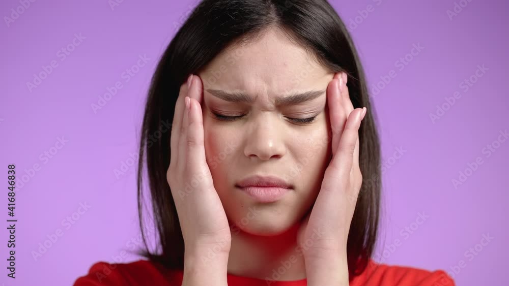 Young woman having headache, studio portrait. Girl putting hands on head, isolated on violet background. Concept of problems, migraine pain, illness Young woman having headache, studio portrait. Girl putting hands on head, isolated on violet background. Concept of problems, migraine pain, illness