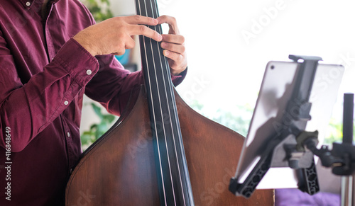 Close up of a young man teaching live music with his tablet. He teaches how to play the double bass