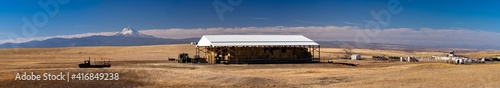 A panorama image of a hay storage barn and farm equipment and rodeo grounds and  on a farm near Dufur Oregon with Mt Hood in the background. © Bob