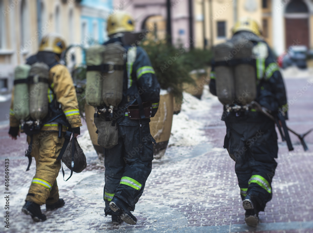 Group of fire men in uniform during fire fighting operation in the city streets, firefighters with the fire engine truck fighting vehicle in the background, emergency and rescue Group of fire men in uniform during fire fighting operation in the city streets, firefighters with the fire engine truck fighting vehicle in the background, emergency and rescue