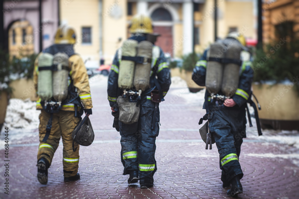 Group of fire men in uniform during fire fighting operation in the city streets, firefighters with the fire engine truck fighting vehicle in the background, emergency and rescue Group of fire men in uniform during fire fighting operation in the city streets, firefighters with the fire engine truck fighting vehicle in the background, emergency and rescue