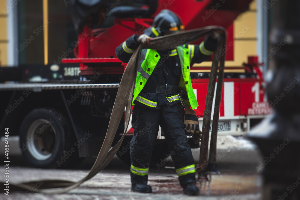 Group of fire men in uniform during fire fighting operation in the city streets, firefighters with the fire engine truck fighting vehicle in the background, emergency and rescue