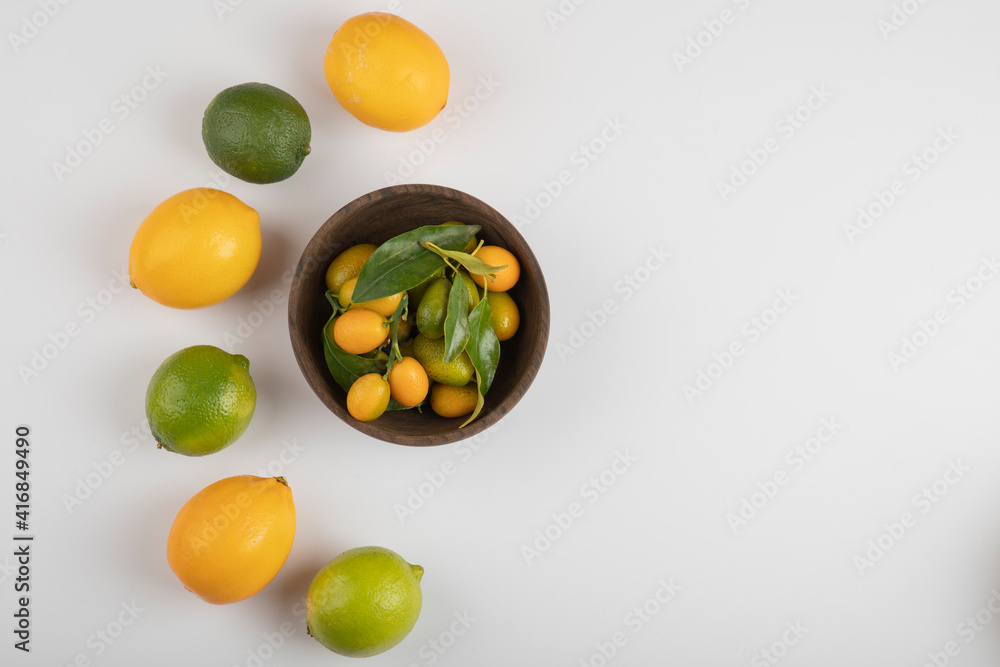 Bowl of fresh kumquats, limes and lemons on white background Bowl of fresh kumquats, limes and lemons on white background