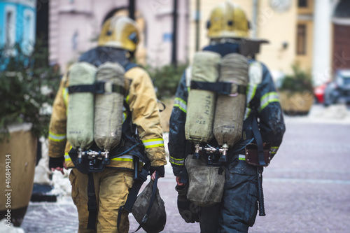 Group of fire men in uniform during fire fighting operation in the city streets, firefighters with the fire engine truck fighting vehicle in the background, emergency and rescue