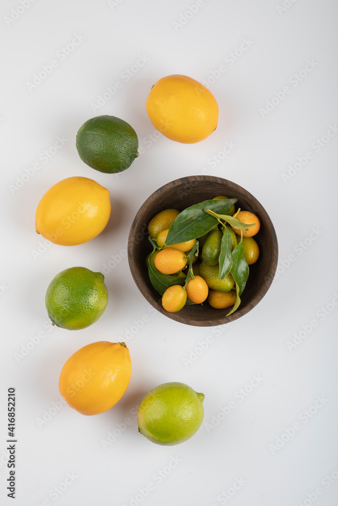 Bowl of fresh kumquats, limes and lemons on white background Bowl of fresh kumquats, limes and lemons on white background