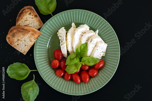 Caprese salad with mozzarella cheese, cherry tomatoes and fresh basil leaves on black background. Top view.