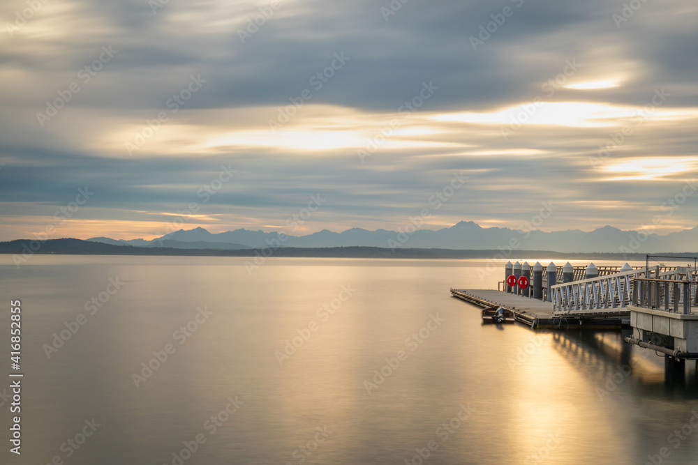 Long exposure photography of the bay in Seattle with a pier during sunset, calm water, golden hour.