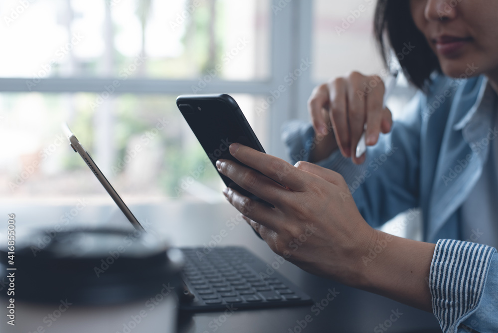 Asian business woman using mobile smart phone for video calling during working on laptop from home Asian business woman using mobile smart phone for video calling during working on laptop from home