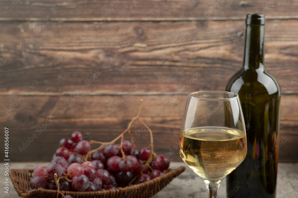 Wicker basket of red grapes with glass of white wine on marble table