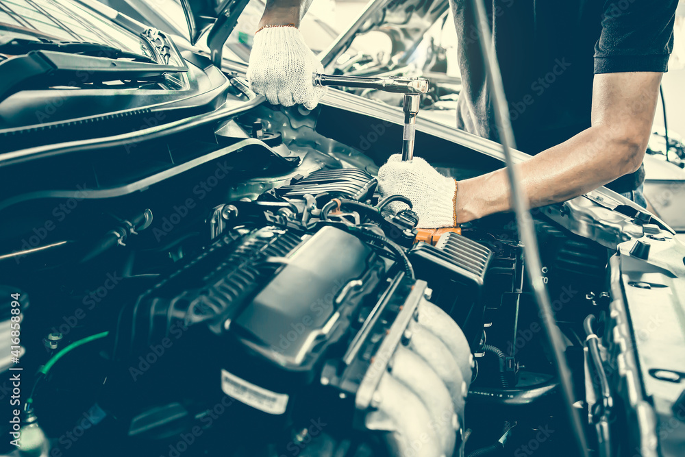 Close-up hands of auto mechanic are using the wrench to repair and maintenance auto engine is problems at car repair shop. Concepts of car care check and fixed and services insurance.