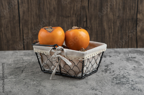 Fototapeta Naklejka Na Ścianę i Meble -  Delicious fuyu persimmon fruits placed in basket on marble surface