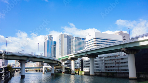 ある晴れた日の青空と雲を背景に高速道路と高層ビルが合わさった風景 © tokoteku_2018