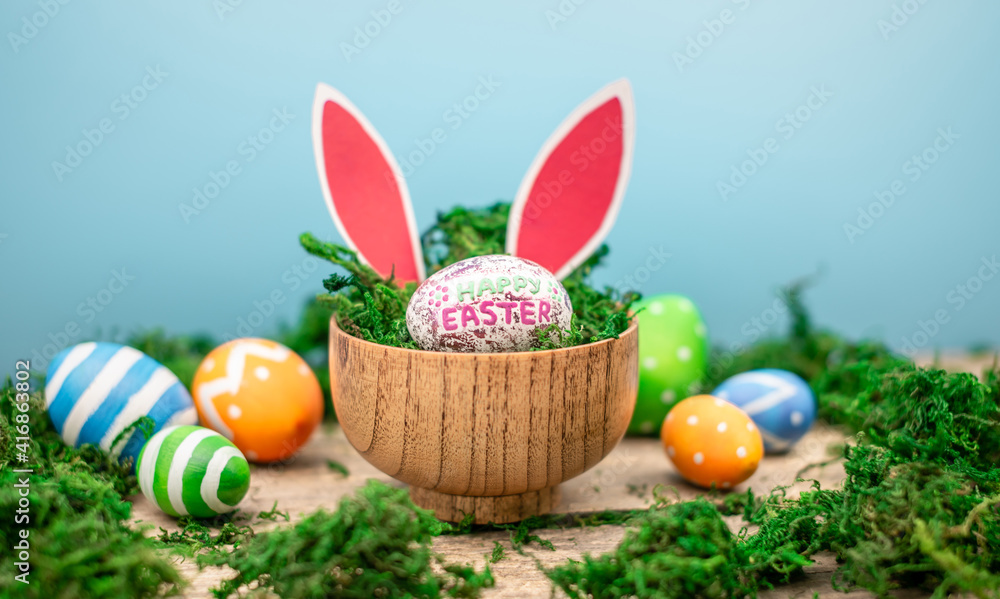 Bright colorful Easter eggs and rabbit ears on a blue and wooden background with green moss