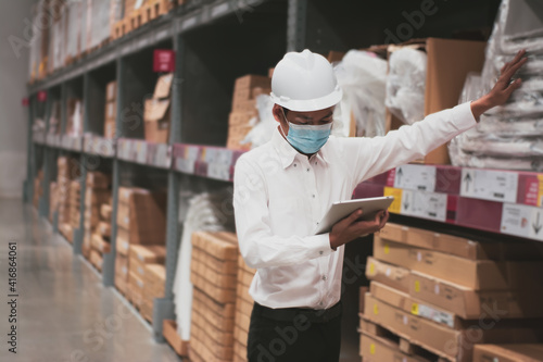 Soft focus asian engineer or technician wearing mask,safety hard hat,uses digital tablet check merchandise stock,security cargo management,in warehouse,industry business logistic and export concept