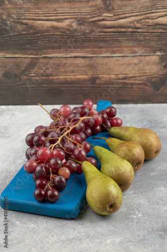 Red grapes on blue cutting board with ripe pears on marble surface