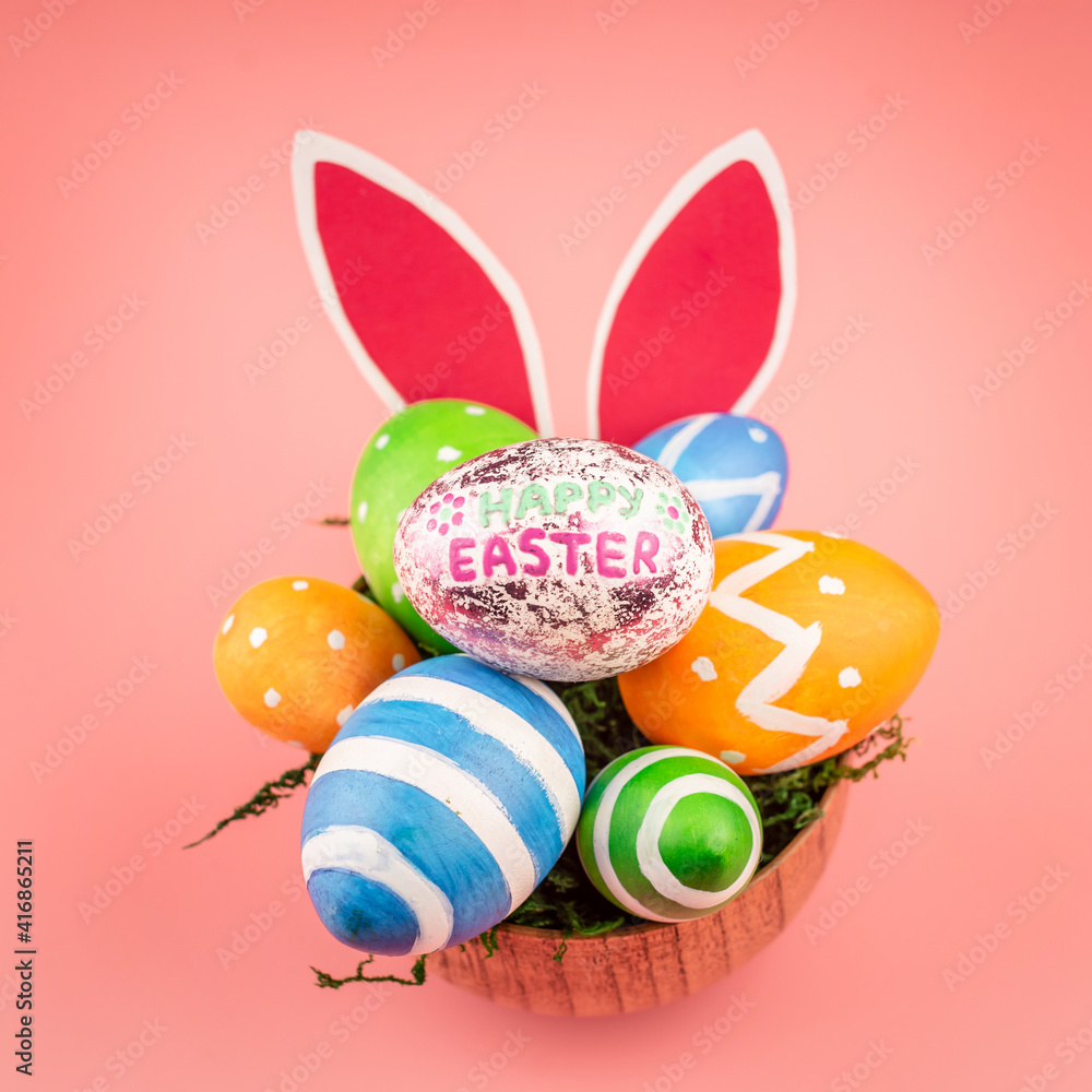 Bright Easter colorful eggs in a wooden bowl, paper rabbit ears on a pink background