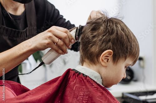 Close-up of woman hands grooming kid boy hair in barber shop. © Екатерина Говорина