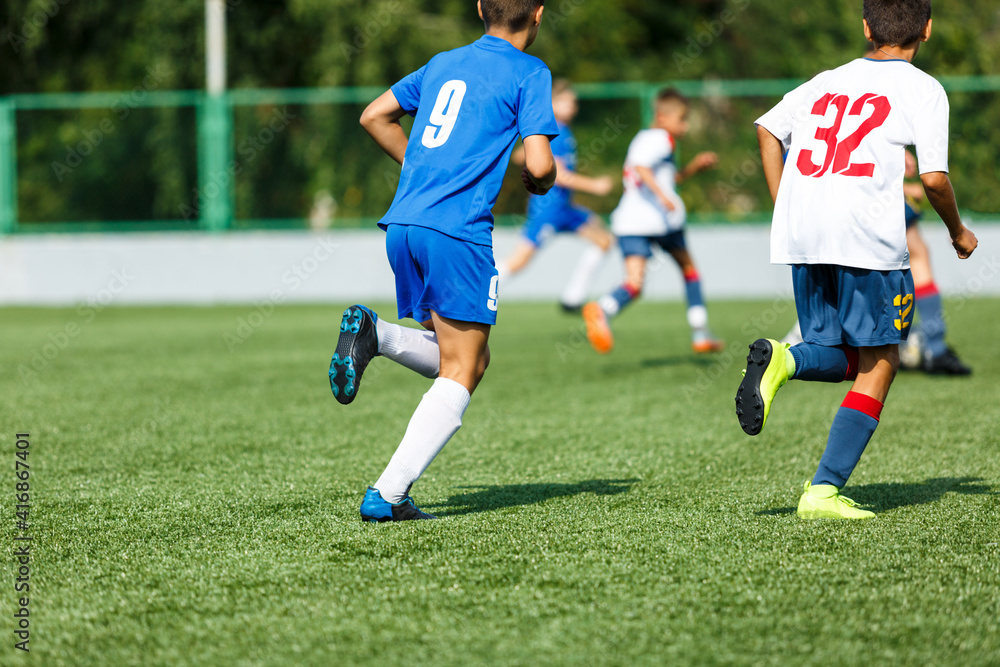 Young sport boys in blue sportswear running and kicking a  ball on pitch. Soccer youth team plays football in summer. Activities for kids, training	