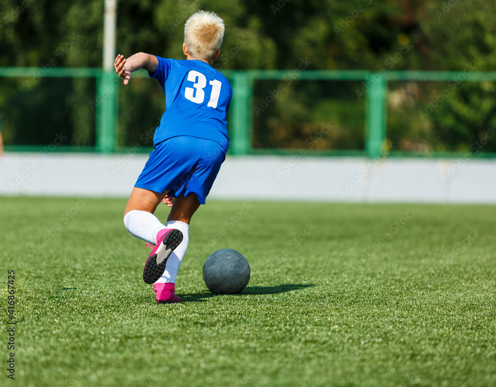 Young sport boys in blue sportswear running and kicking a ball on pitch. Soccer youth team plays football in summer. Activities for kids, training Young sport boys in blue sportswear running and kicking a ball on pitch. Soccer youth team plays football in summer. Activities for kids, training