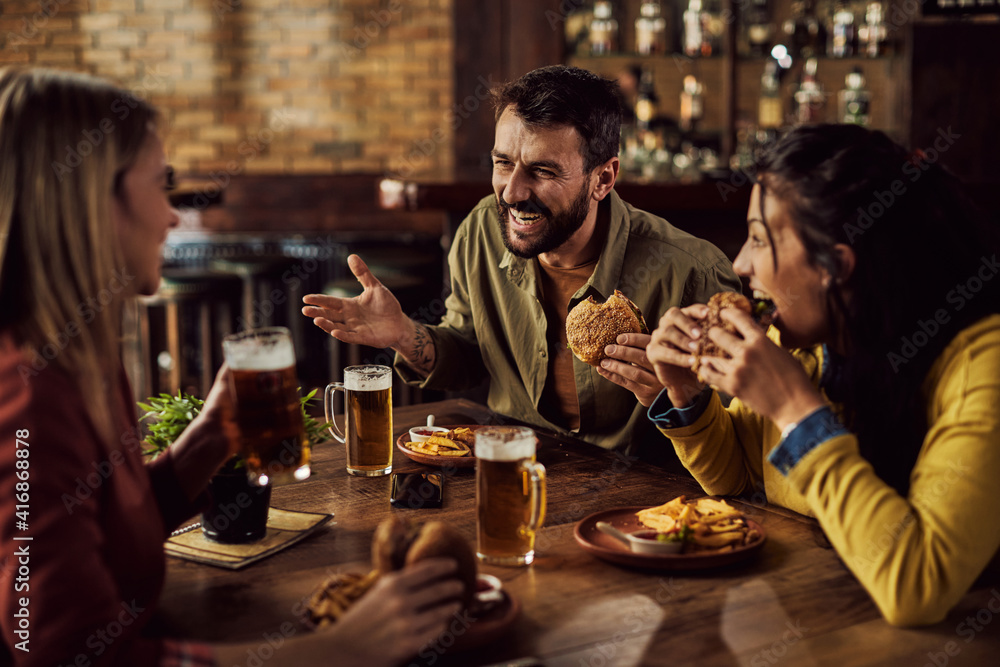 Cheerful friends talking while drinking beer and eating in a pub.