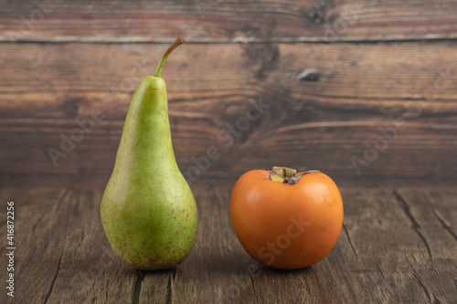 Single whole pear and delicious persimmon on wooden background