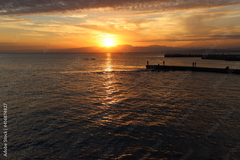 片瀬江ノ島海岸から見る伊豆半島に沈むオレンジ色の夕日と堤防のシルエット