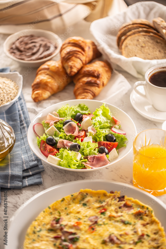 Broad assortment of food including omelette, croissants, salad, bread, oatmeal, jam, waffles, honey, choclate spread, coffee and orange juice served on a table Broad assortment of food including omelette, croissants, salad, bread, oatmeal, jam, waffles, honey, choclate spread, coffee and orange juice served on a table