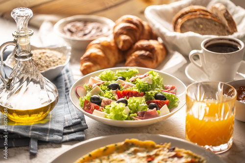 Broad assortment of food including omelette, croissants, salad, bread, oatmeal, jam, waffles, honey, choclate spread, coffee and orange juice served on a table