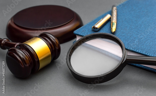 Magnifying glass with judge gavel and notepad on black background.
