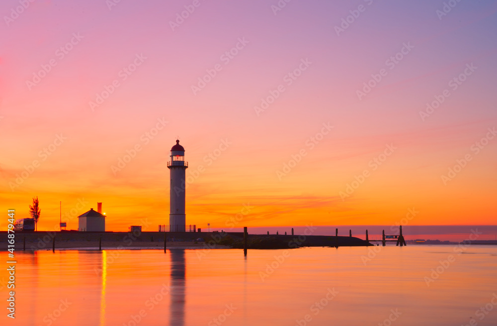 Silhouette of a lighthouse by the sea under orange sunset sky