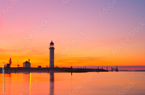 Silhouette of a lighthouse by the sea under orange sunset sky
