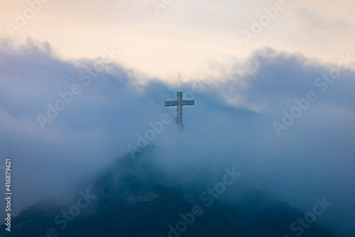 Obraz na płótnie A single cross stands on a mountain engulfed in white clouds w salonie