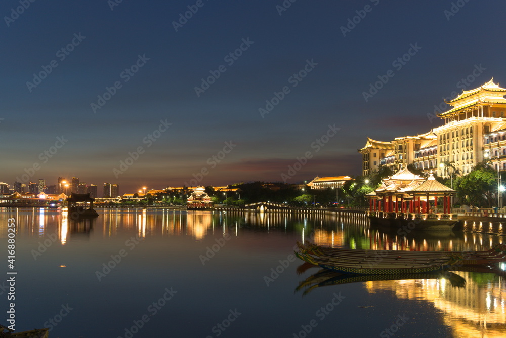 Bright city buildings at night. Dragon boat parked on water