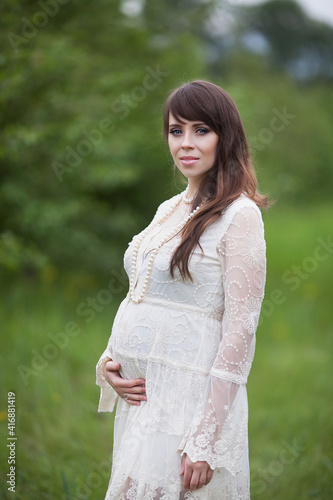 Happy pregnant woman in a beautiful stylish white dress against the background of nature