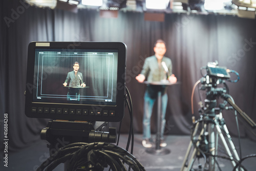 Young journalist in a television recording studio is talking into a microphone, blurry film cameras