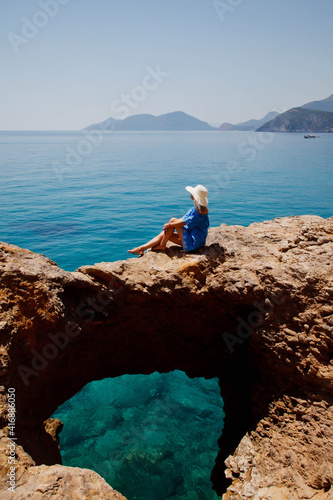 Young woman enjoying holiday on rock with luxury view walking showing emotion on azure sea background. Happy female on romantic trip have fun on summer vacation. Concept romance and relaxation