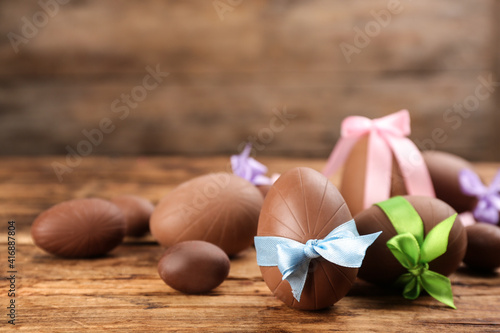 Sweet chocolate eggs with bows on wooden table. Space for text
