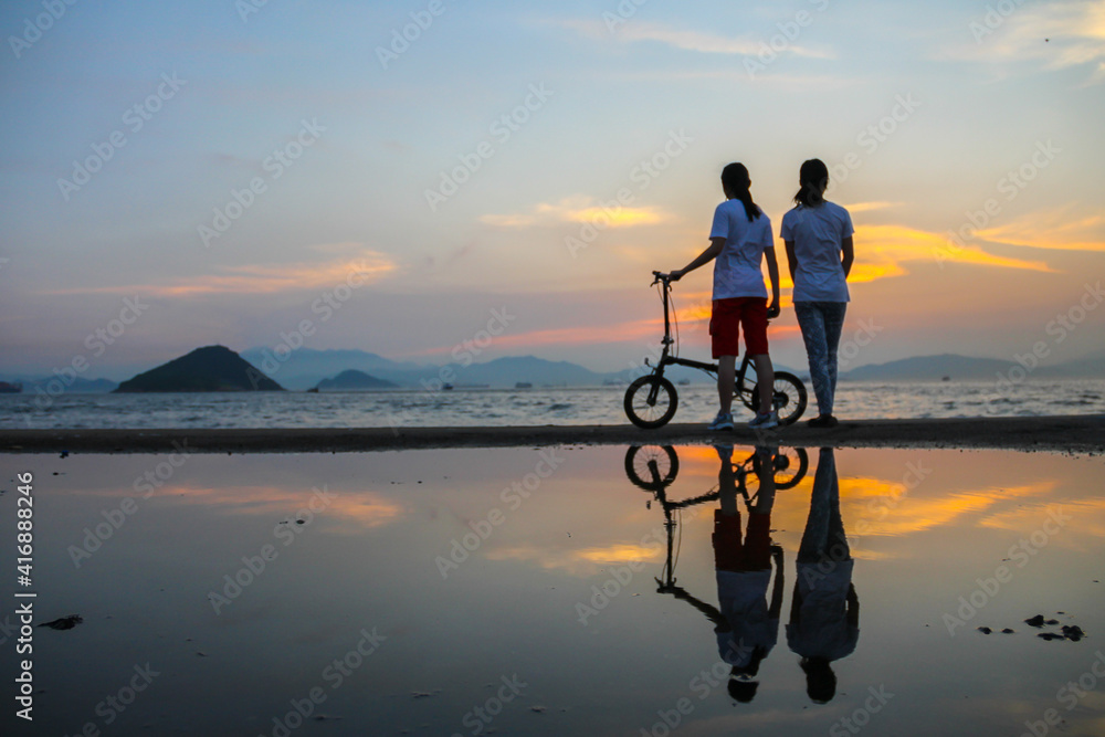 reflection of two girls and a bicycle at Sunset at Water front at Western District Public Cargo Working Area, Kennedy town, Victoria Harbour, Hong Kong.