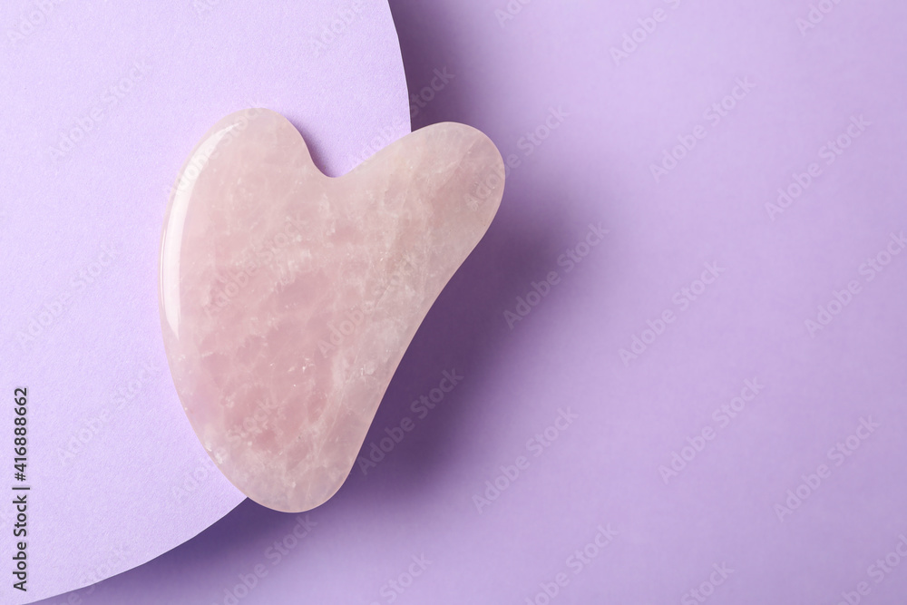 Fototapeta premium Rose quartz gua sha tool on violet background, top view. Space for text