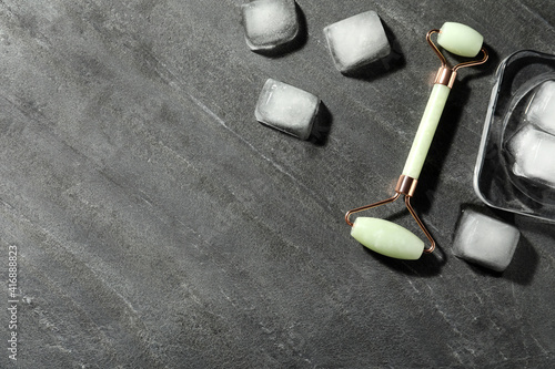 Natural jade face roller and ice cubes on grey background, flat lay. Space for text