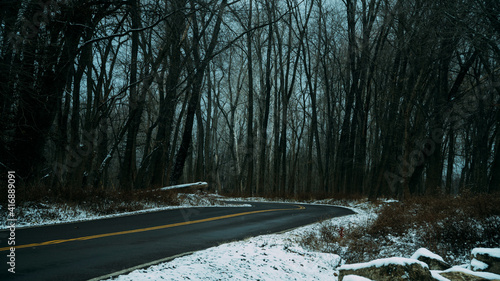 Small, two-lane road leading through forested area during winter, with snow on either side.