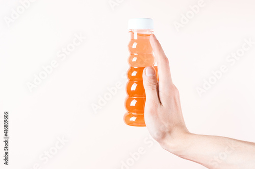 Fingers hold a jar of baby toy slime. Orange honey on a beige background