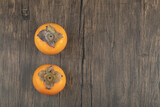 Two ripe persimmon fruits placed on wooden surface