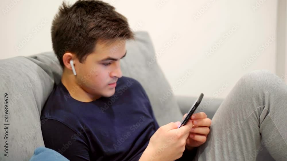 A young man with a smartphone in his hands sits on the couch. A young man with a smartphone in his hands sits on the couch.