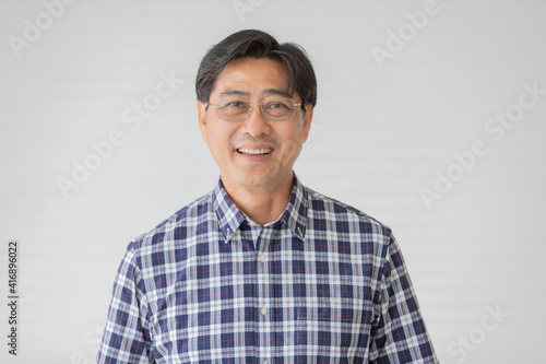 Portrait close up shot of middle aged asian male model with short black hair wearing blue plaid shirt with stand smiling in front of white background