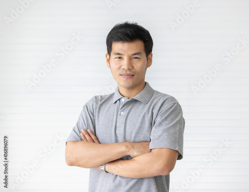 Portrait close up shot of handsome asian male model with short black hair wearing gray polo shirt stand smiling in front of white background