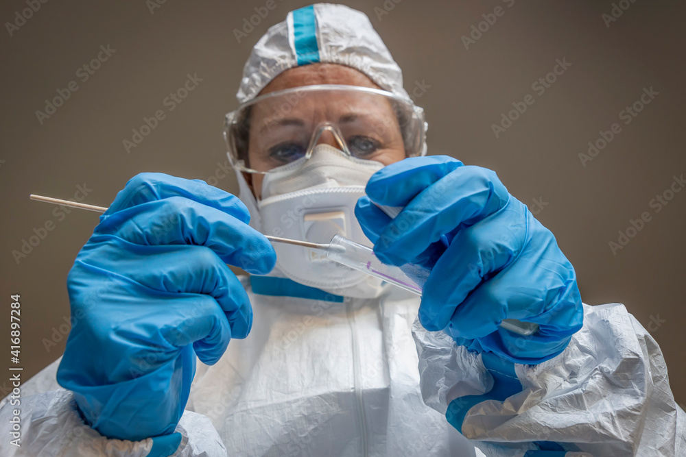 A woman, laboratory technician, completely covered in a white protective suit, makes a test swab to check for a possible infection with Coronavirus Covid-19 A woman, laboratory technician, completely covered in a white protective suit, makes a test swab to check for a possible infection with Coronavirus Covid-19
