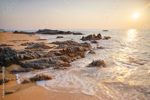 Beautiful sunset seascape with rock on sand beach.